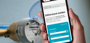 Ein Smartphone zeigt die Kundenwebsite von Veolia auf der Zählerstände übermittelt werden können. Im Hintergrund ist ein Wasserzähler zu sehen, deren Zifferblatt deutlich erkennbar ist. Das Bild illustriert die M Moderne, digitale Methode zur Übermittlung von Wasserverbrauchsdaten.