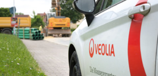 Veolia-Fahrzeug auf einer Baustelle in Döbeln. Im Hintergrund gelbe Baumaschinen und grüne Rohre.