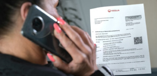 Eine Frau hält ein Smartphone am Ohr und hält dabei einen Brief in der Hand.