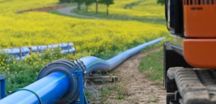 Eine blaue Trinkwasserleitung liegt auf einer Wiese. Daneben sieht man die Räder eines Baustellenfahrzeugs.