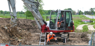 Ein rot-weißer Bagger auf der die Erde des Bodens ausbaggert.